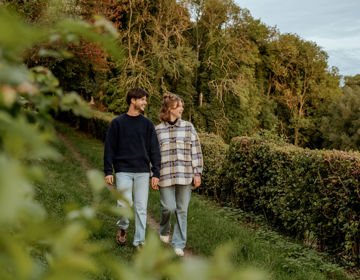 Een jong koppel wandelt over een pad met heg en kijkt uit over een herfstlandschap