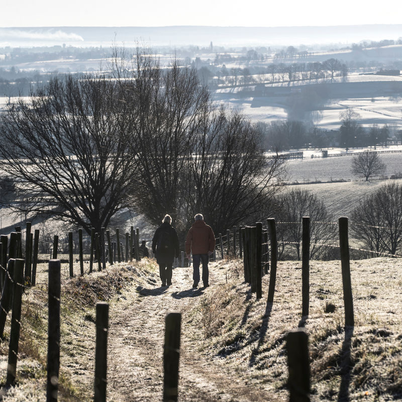 Twee wandelaars lopen een heuvel af in een winters landschap bij Epen