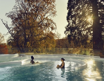 Twee dames zitten in thermaal buitenbad met uitzicht over de herfstige kleuren van de natuur