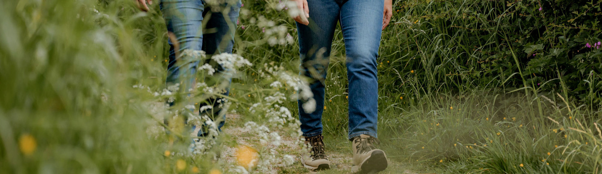 Twee wandelaars lopen door een dicht begroeid wandelpaadje