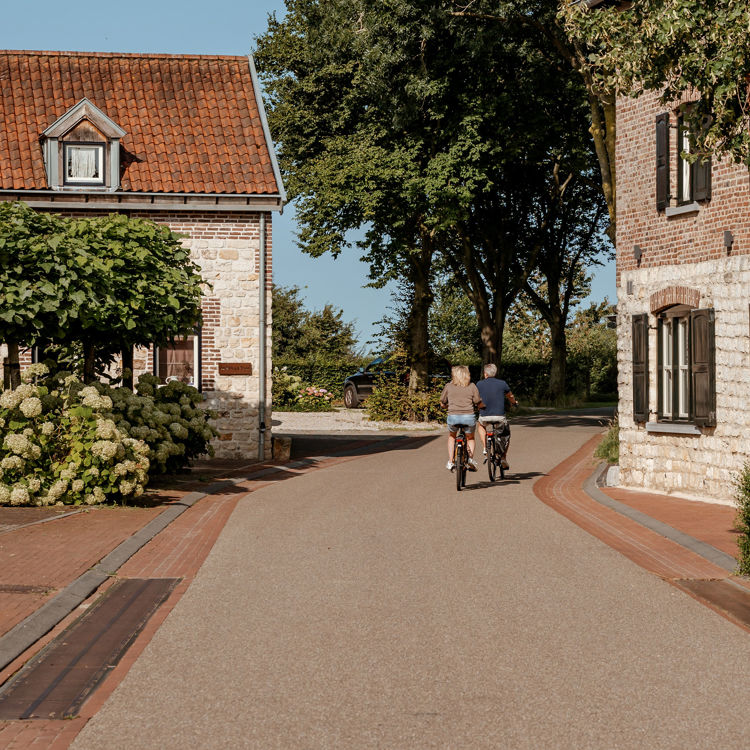 Koppel fietst door smal straatje met mergelwoningen in Colmont aan beide kanten. 
